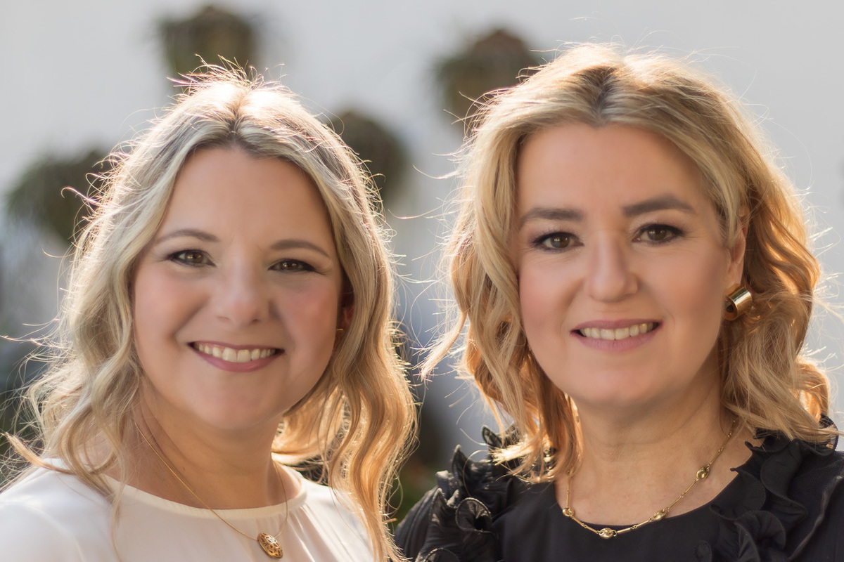 duas irmãs. somente o rosto. ambas loiras cabelo até os ombros repartido no meio. ambas sorrindo. uma de blusa preta e outra de blusa branca