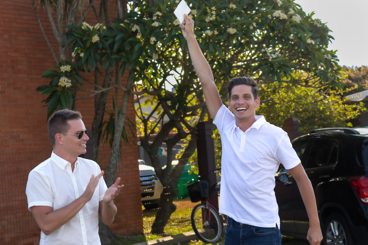 irmão comemorando o convite de ser padrinho de casamento. com o braço erguido segurando o convite