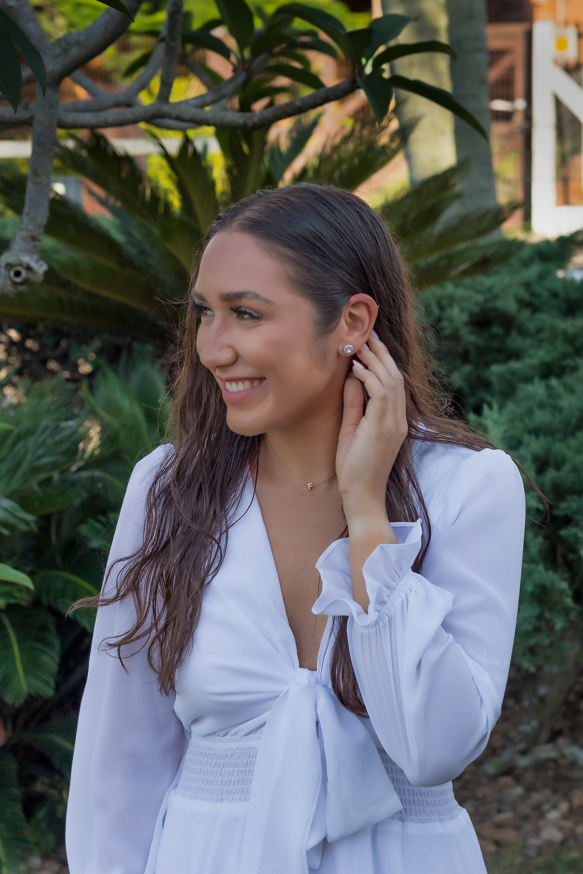 garota colocando cabelo atras da orelha com a mão esquerda e olhando levemente para a direita. esta com vestido branco