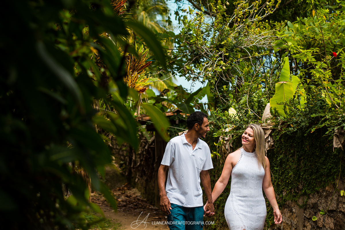 casal de noivos andando de mãos dadas e sorrindo em trilha em ensaio pré-wedding pré casamento na praia em Ubatuba litoral norte de são paulo