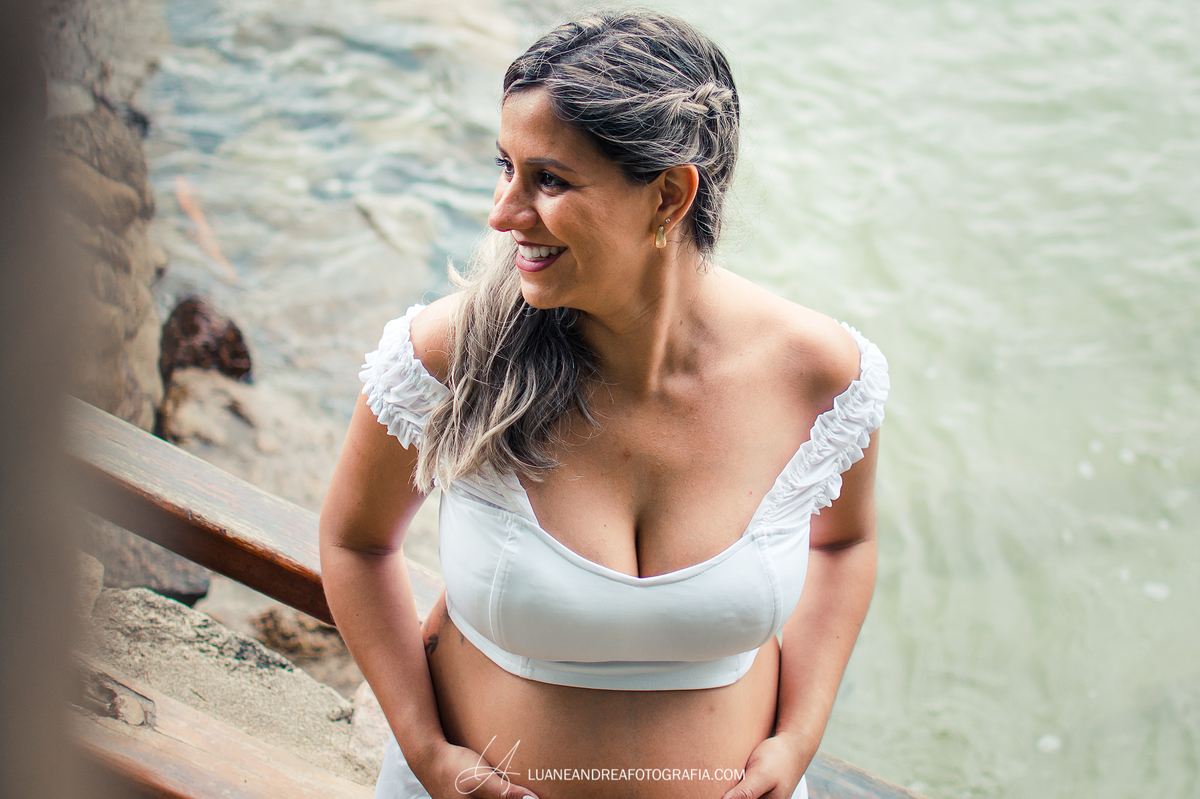 mulher grávida sorrindo e segurando a barriga na praia em ensaio gestante em ubatuba são paulo