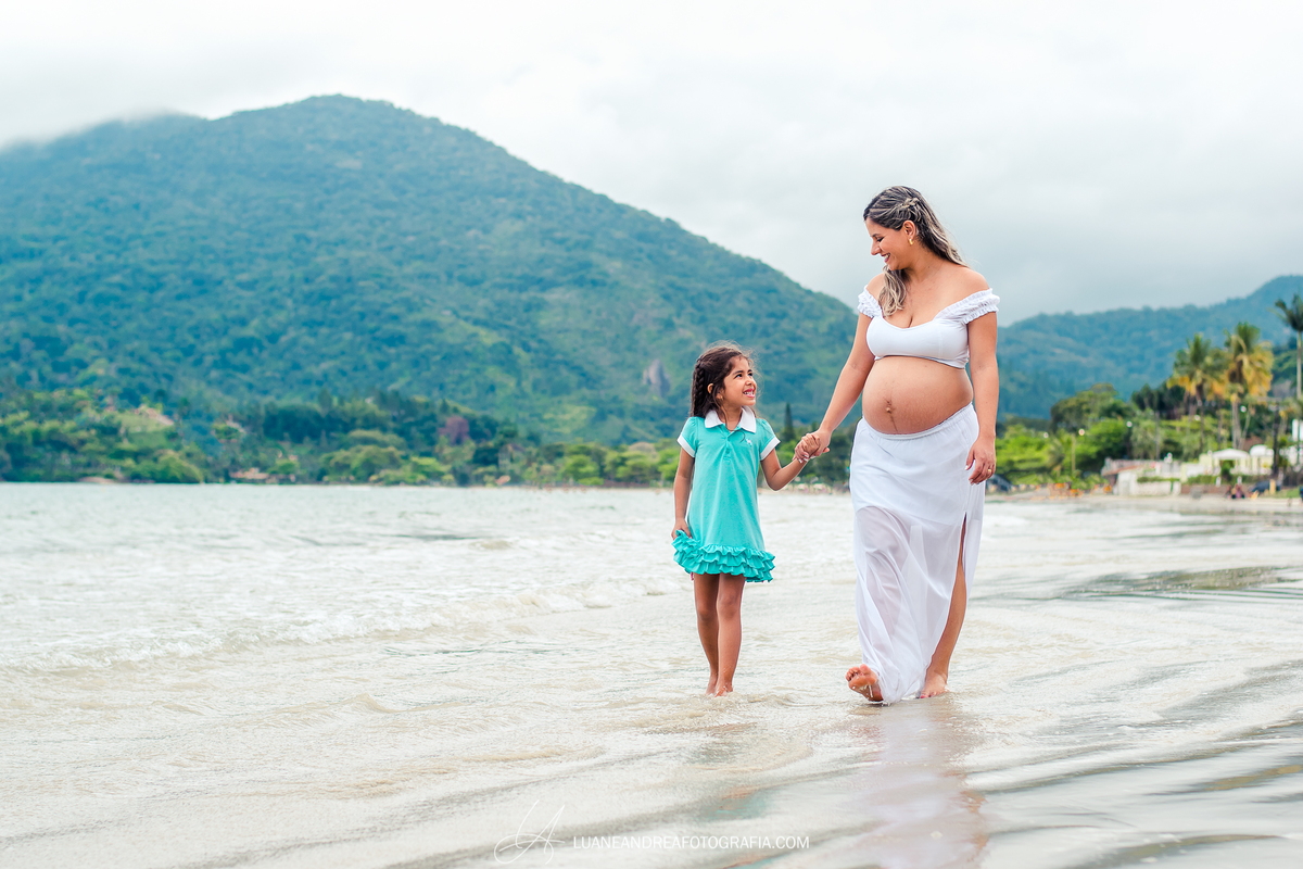 mulher grávida caminhando com a filha na praia em ensaio gestante em ubatuba são paulo