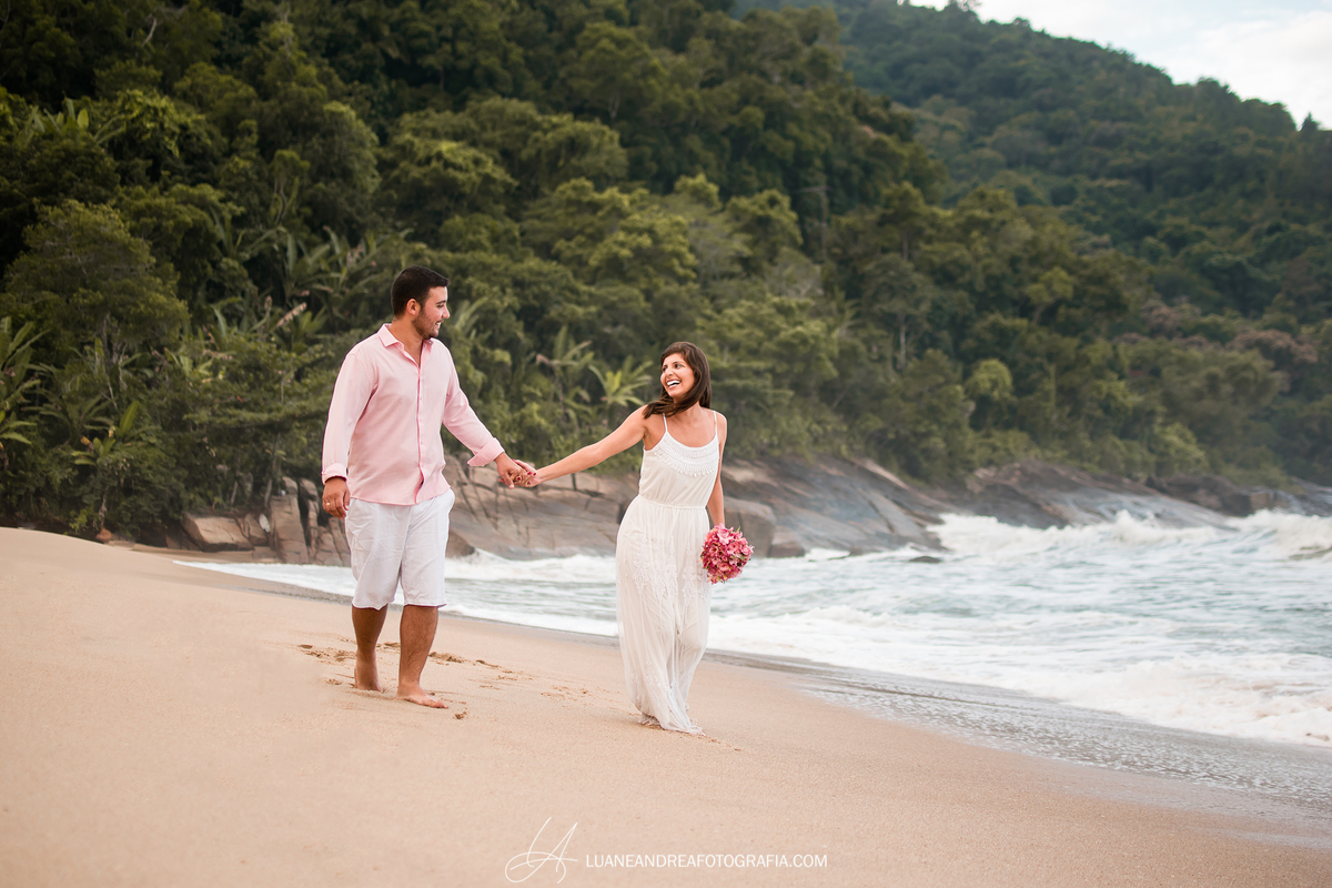 casal de noivos caminhando de mãos dadas e sorrindo em ensaio pré-wedding pré casamento na praia fim de tarde em ubatuba litoral norte de são paulo