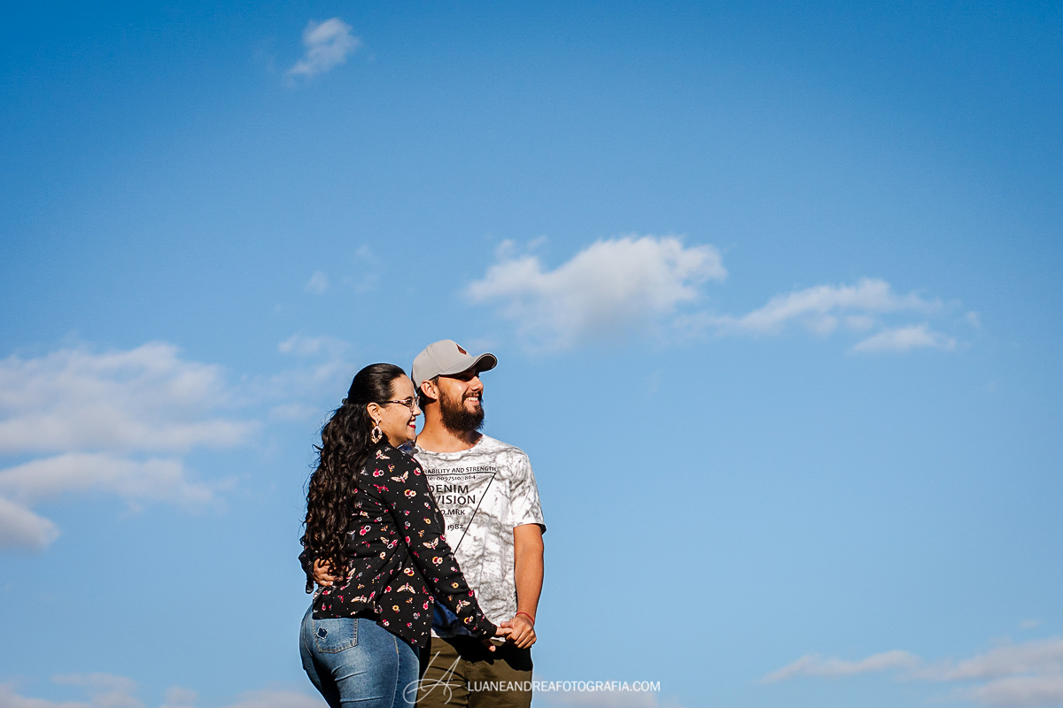 casal abraçado de mãos dadas sorrindo e olhando para o horizonte em ensaio pré wedding casamento no campo em taubaté são paulo