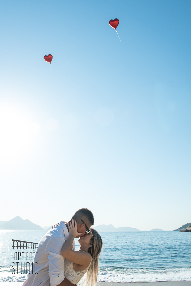 Noivos se beijam com balões de coração ao fundo