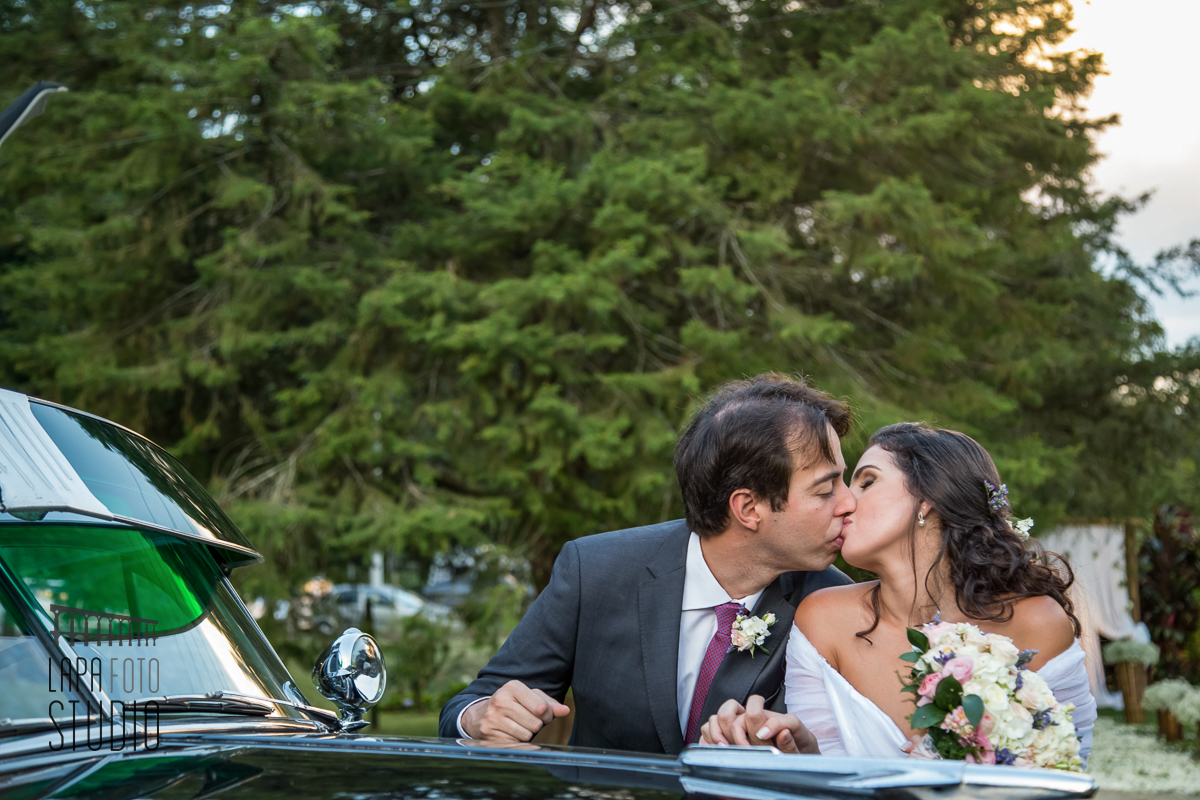 Foto do casal se beijando apoiados no carro antigo para casamentos, logo após a cerimônia de casamento em Friburgo.