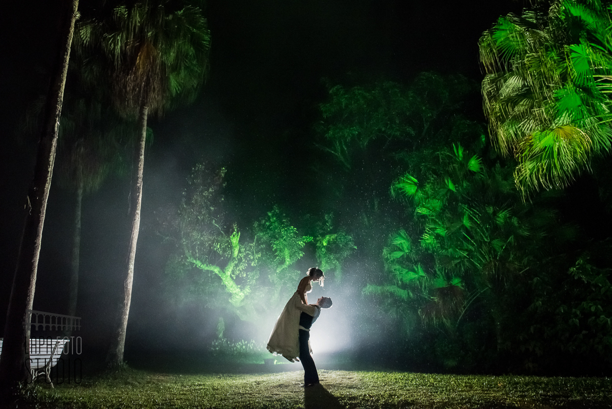 Foto em contraluz do noivo pegando a noiva no colo na chuva no dia do casamento
