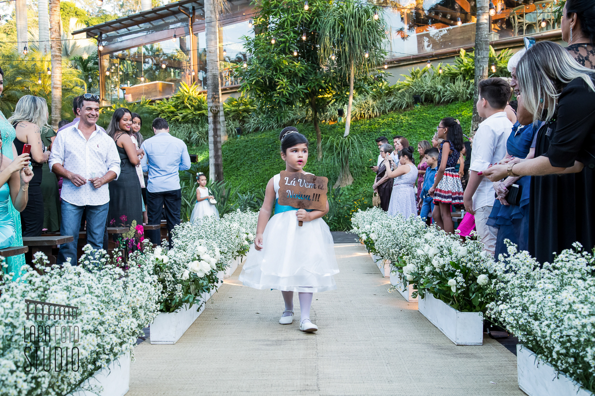 Daminha entra na cerimônia segurando uma placa escrita lá vem a noiva