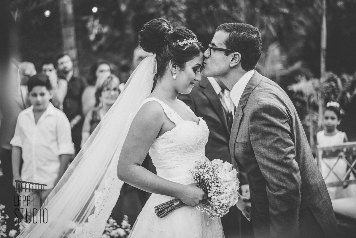 Foto em preto e branco do noivo beijando a testa da noiva após a entrada na cerimônia do casamento