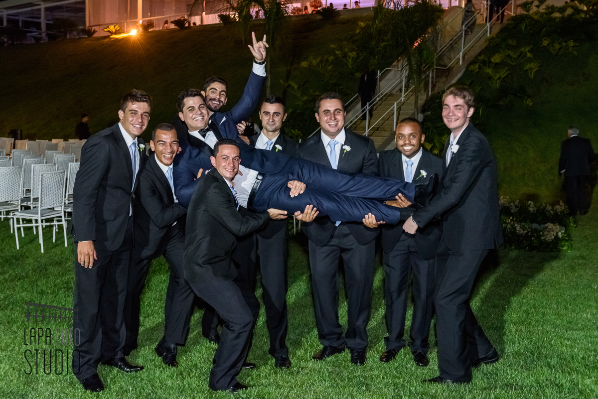 Padrinhos carregam o noivo no colo durante sessão de fotos posadas após o casamento