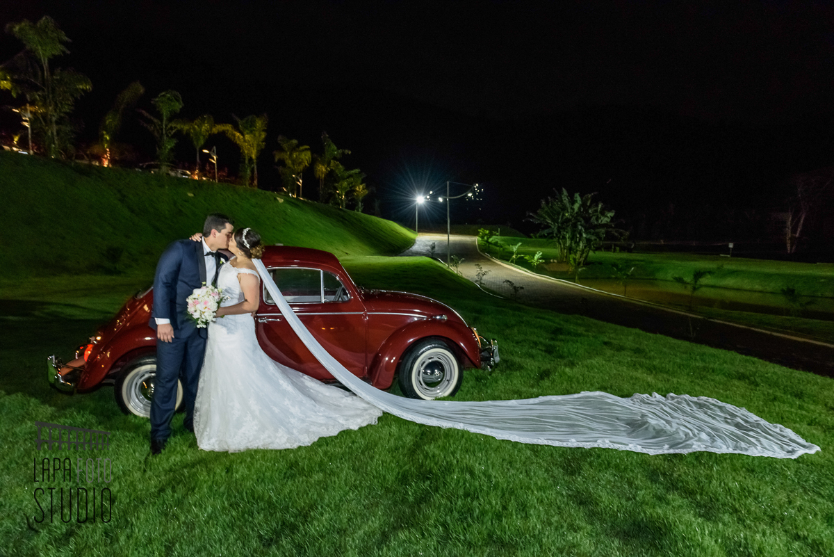 Noivos se beijam com fusca vermelho ao fundo durante ensaio do casal após a cerimônia de casamento