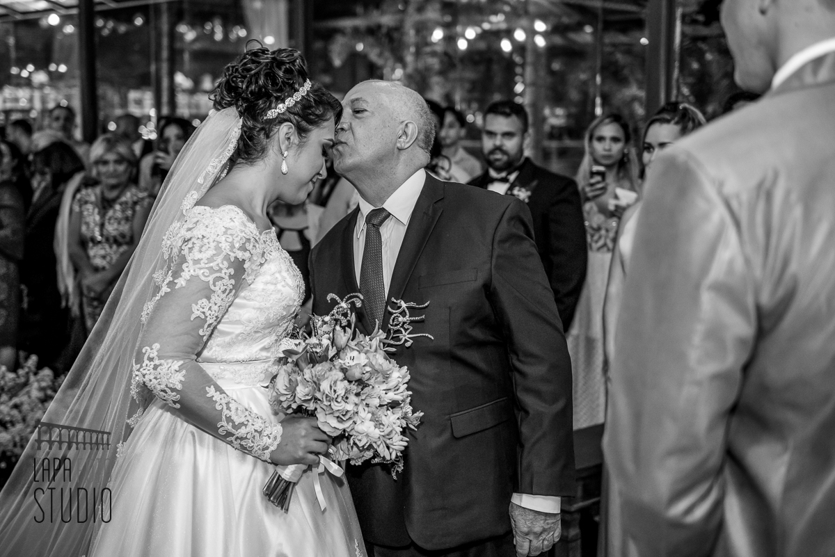 Foto em preto e branco do pai beijando a noiva durante a entrada para cerimônia de casamento