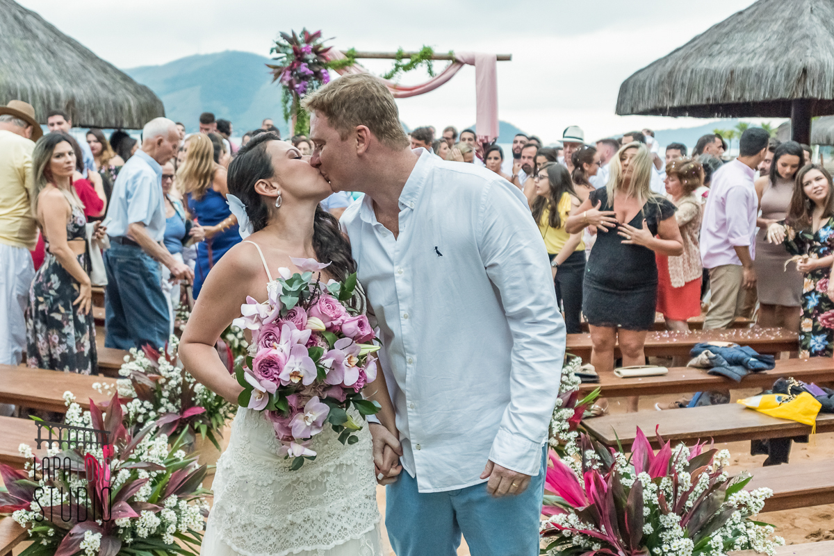 Noivos trocam beijos na saída da cerimônia de casamento na areia