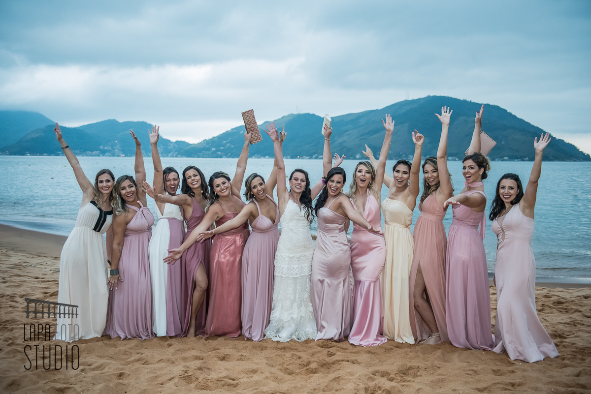 Noiva comemorando com as madrinhas na areia da praia durante fotos posadas pós casamento
