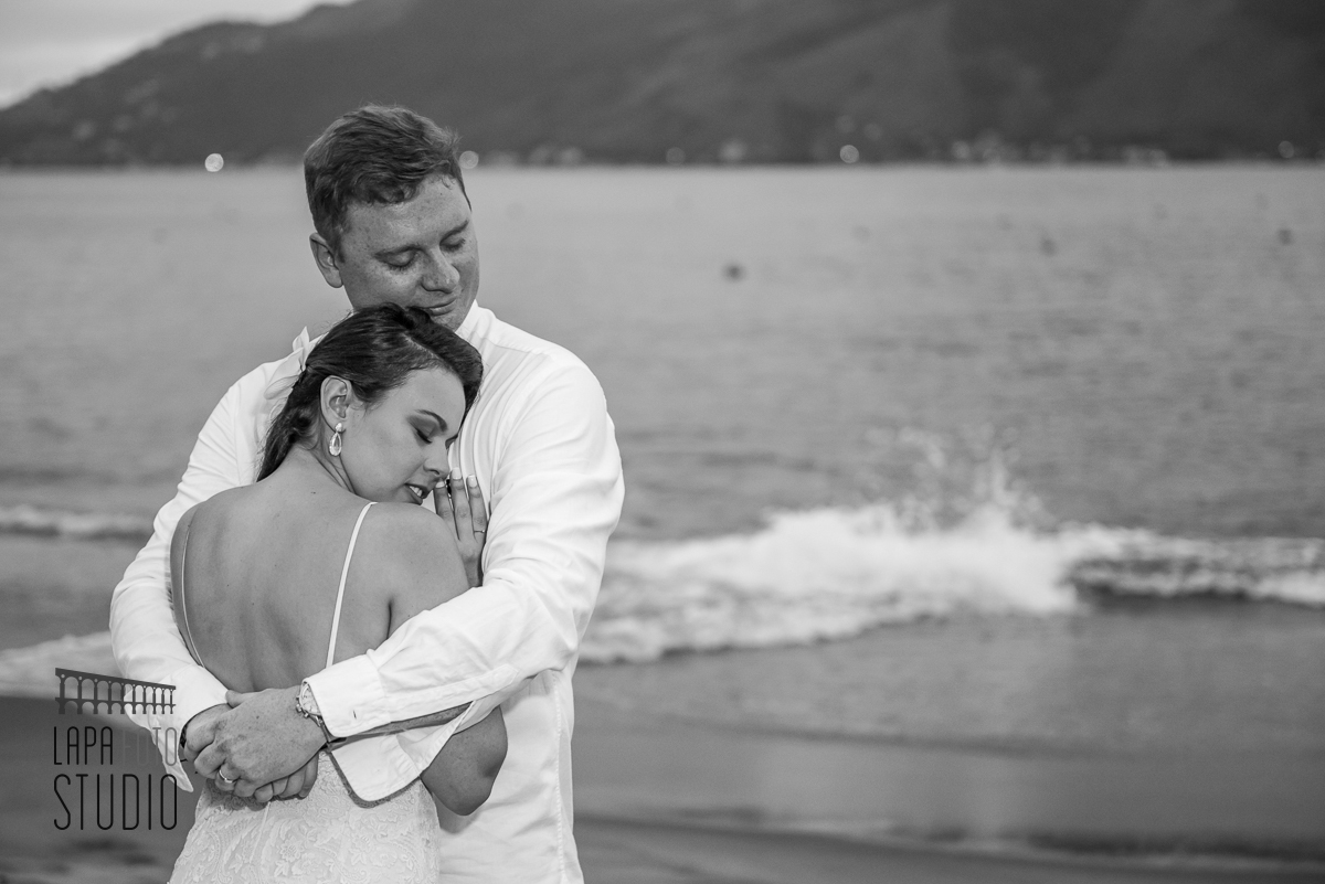 Foto em preto dos noivos abraçados com mar ao fundo durante ensaio do casal pós cerimonia de casamento