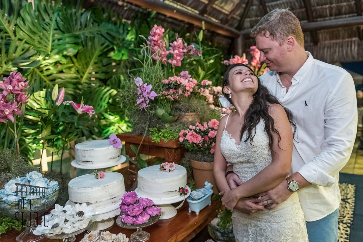 Noivos cortam o bolo juntos e trocam olhares posados na mesa decorada por Patricia Beltrame