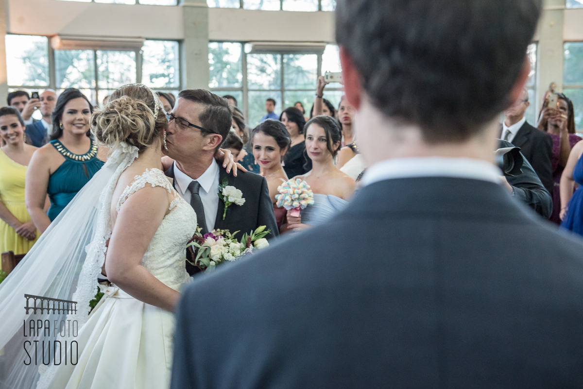 Noiva ganha um beijo do pai pela perspectiva do noivo durante sua entrada na cerimônia de casamento