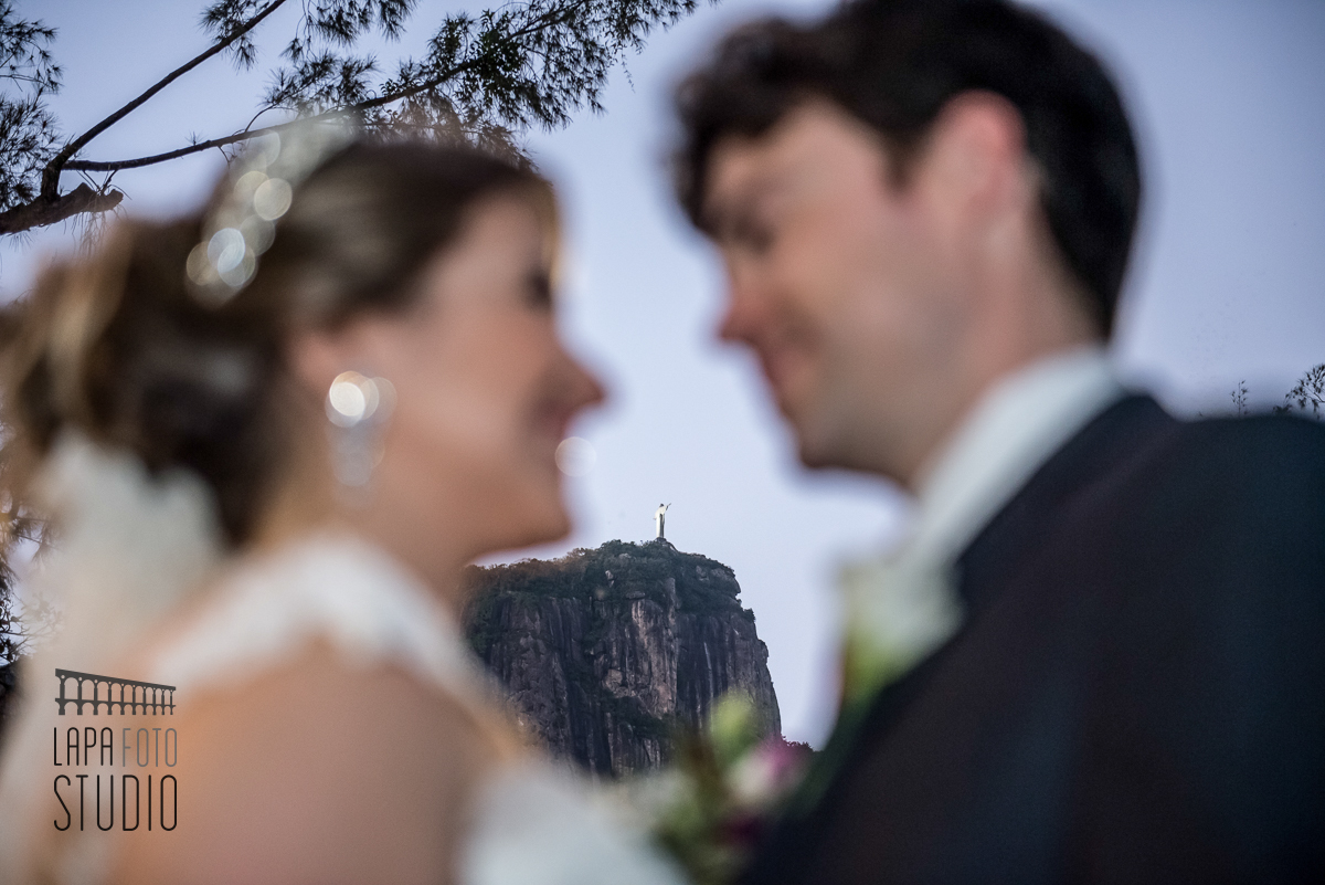 Noivos trocam olhares com Cristo Redentor focado ao fundo durante ensaio pós casamento na Lagoa