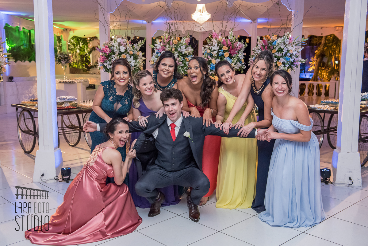 Noivo com as madrinhas agarrando ele numa foto divertida no dia do casamento