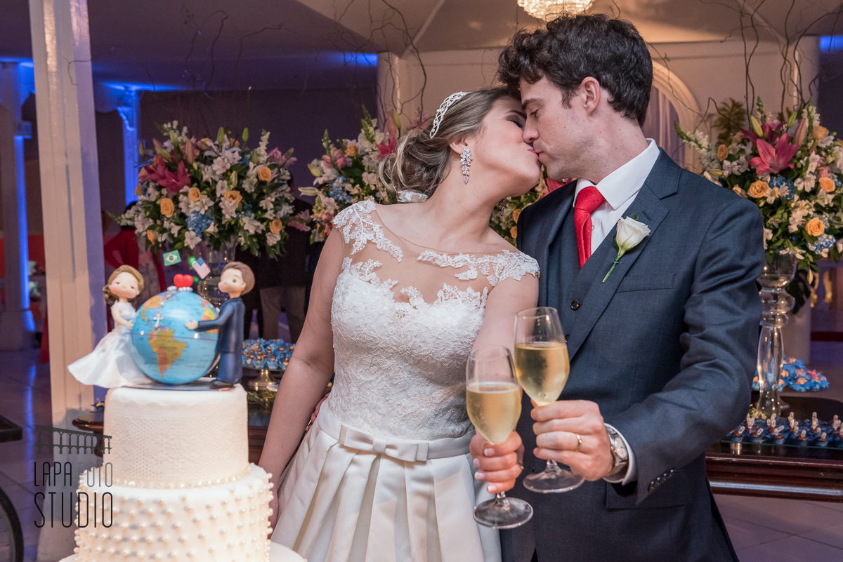 Casal troca um beijo e brinda na mesa do bolo no ensaio pós cerimônia de casamento