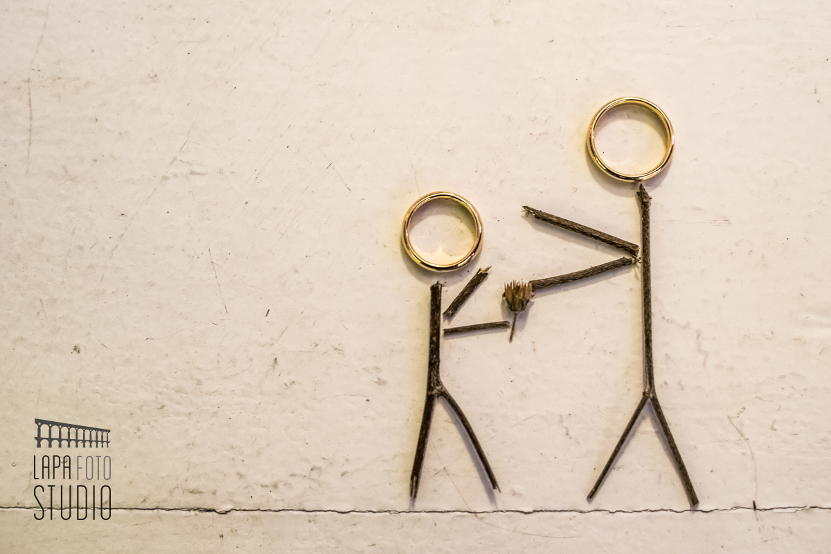 Montagem criativa das alianças de casamento com galhos do buquê da noiva formando dois bonequinhos palito