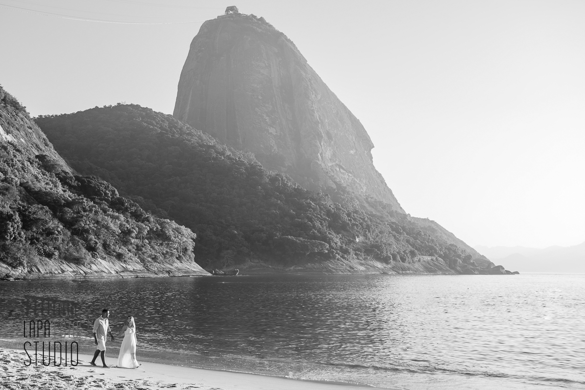 Foto em preto e branco dos noivos caminhando na areia da praia vermelha no ensaio pré casamento