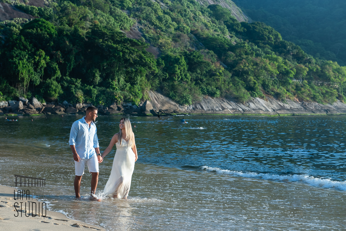 Noivos caminhando na beirada da água da praia vermelha no ensaio pré casamento