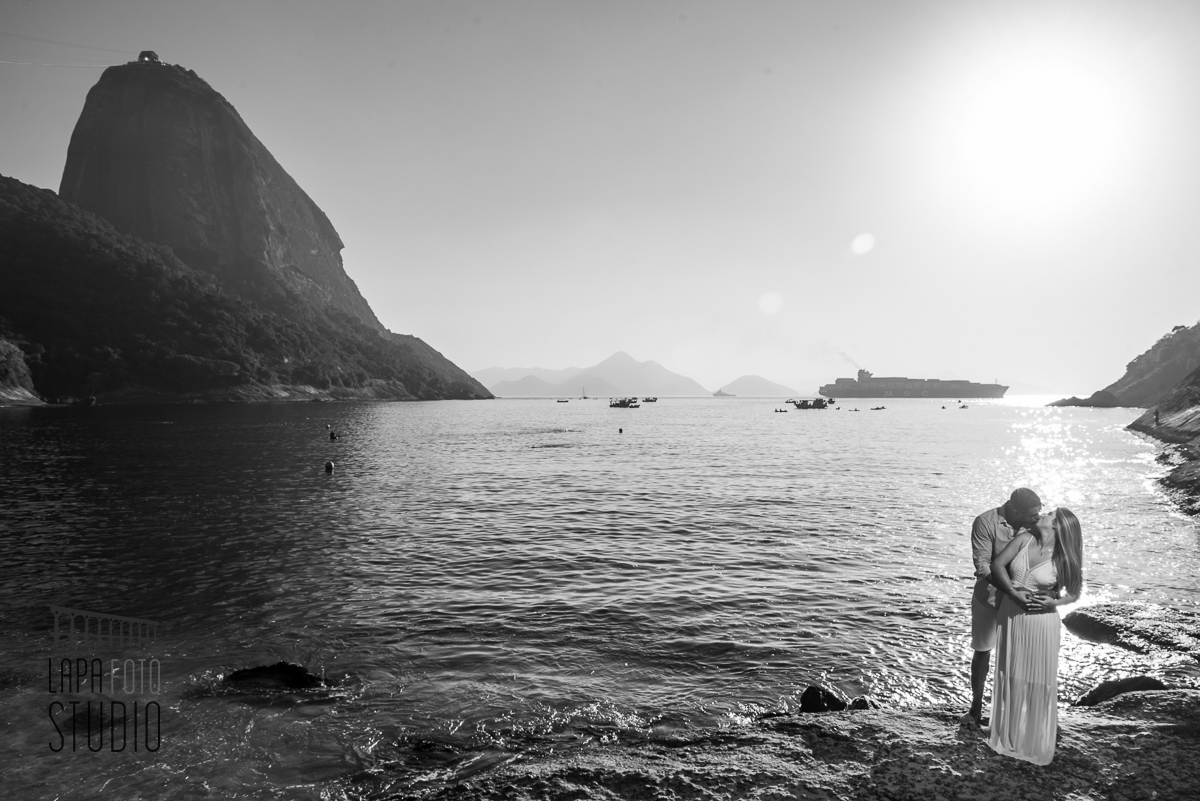 Foto em preto e branco dos noivos em cima de uma pedra na praia vermelha no pré wedding