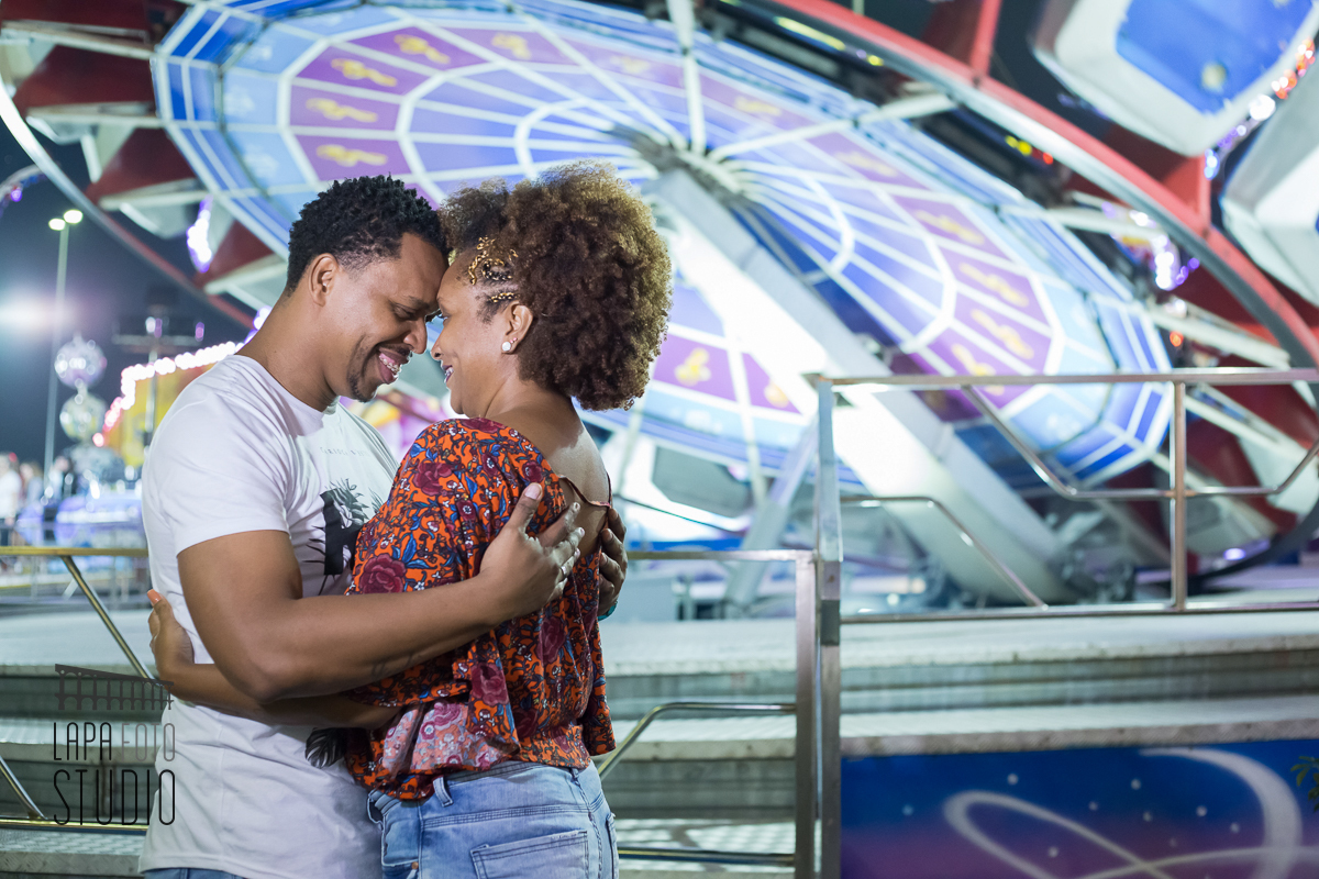 Noivos trocam carinhos com brinquedo iluminado ao fundo no pré wedding no parque