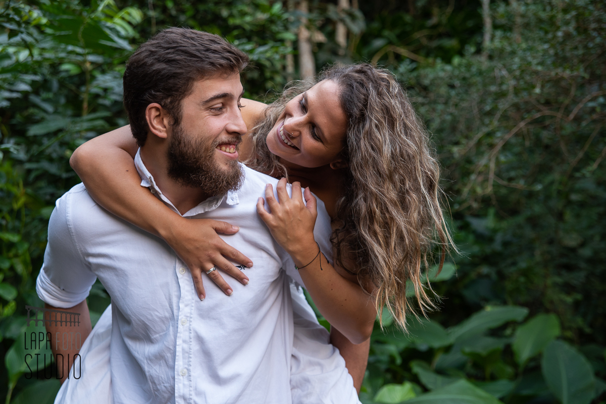 Noiva se debruça nas costas do noivo no dia do pré wedding