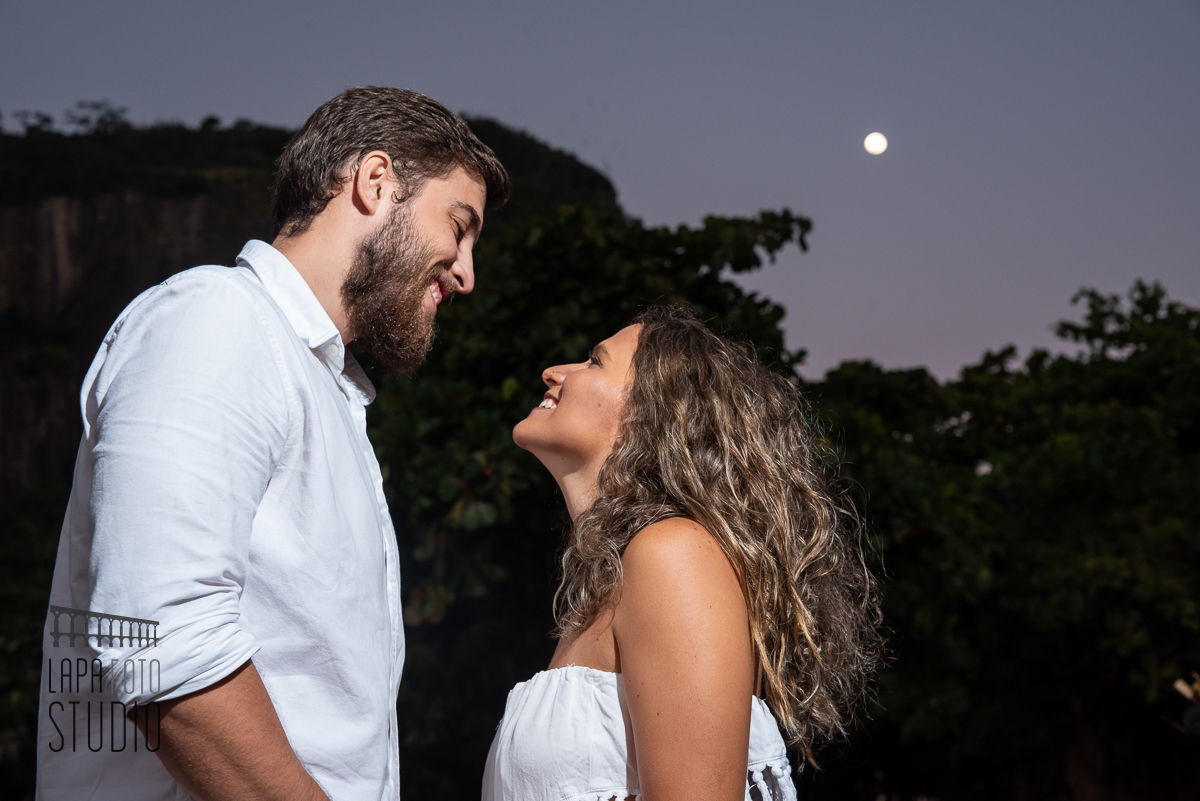 Noivos sorrindo com lua ao fundo no ensaio pré casamento na praia vermelha