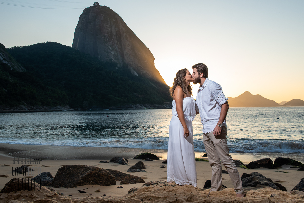 Noivos trocam beijos em cima da pedra na praia vermelha com pão de açúcar ao fundo