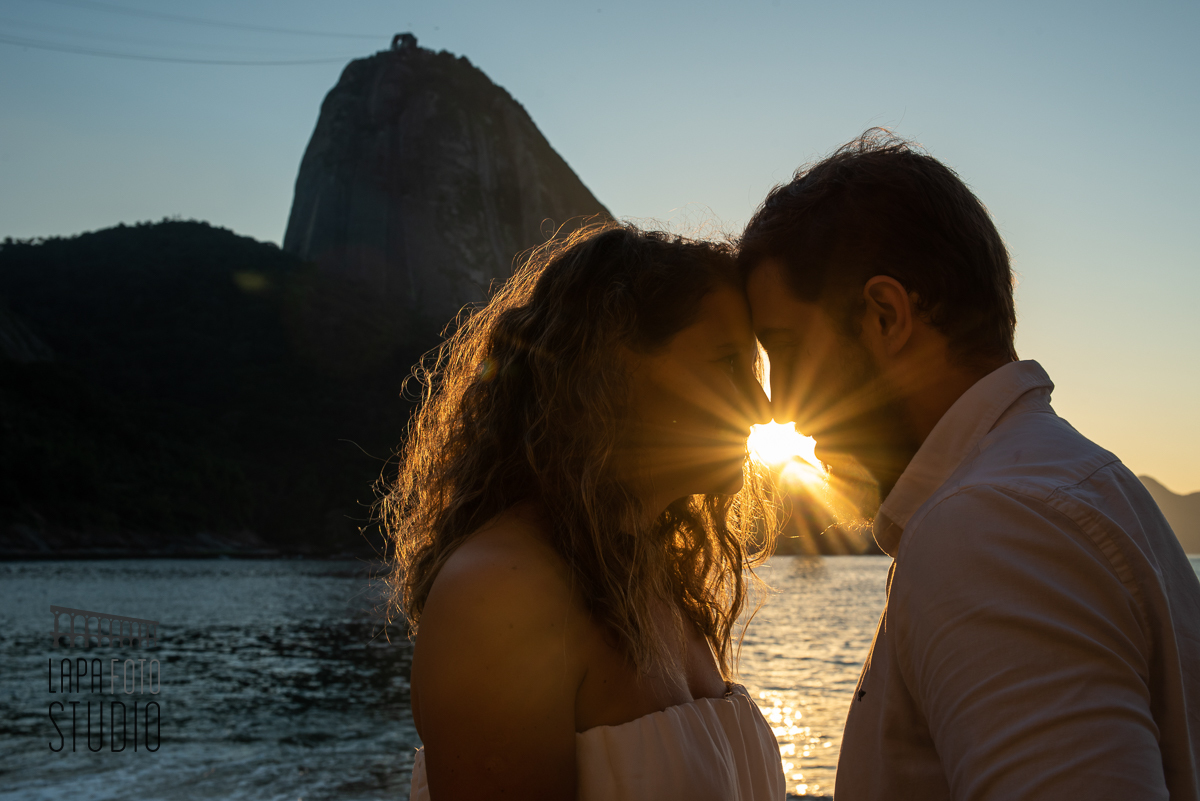 Noivos com testa encostada e sorrindo com sol nascendo ao fundo no pré wedding