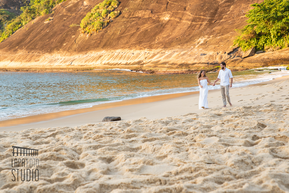 Noivos caminham na areia da praia vermelha no dia do ensaio pré casamento
