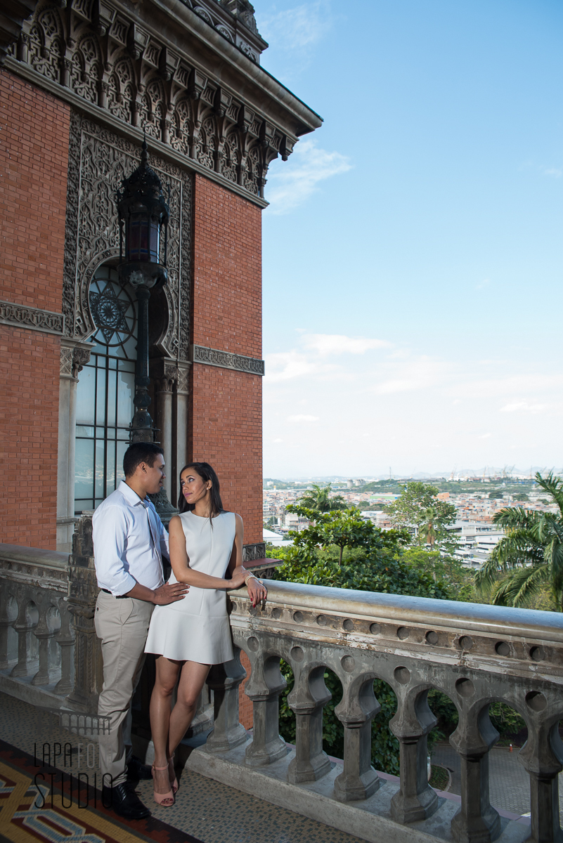 Noivos trocam olhar encostados na varanda da Fiocruz com céu azul ao fundo