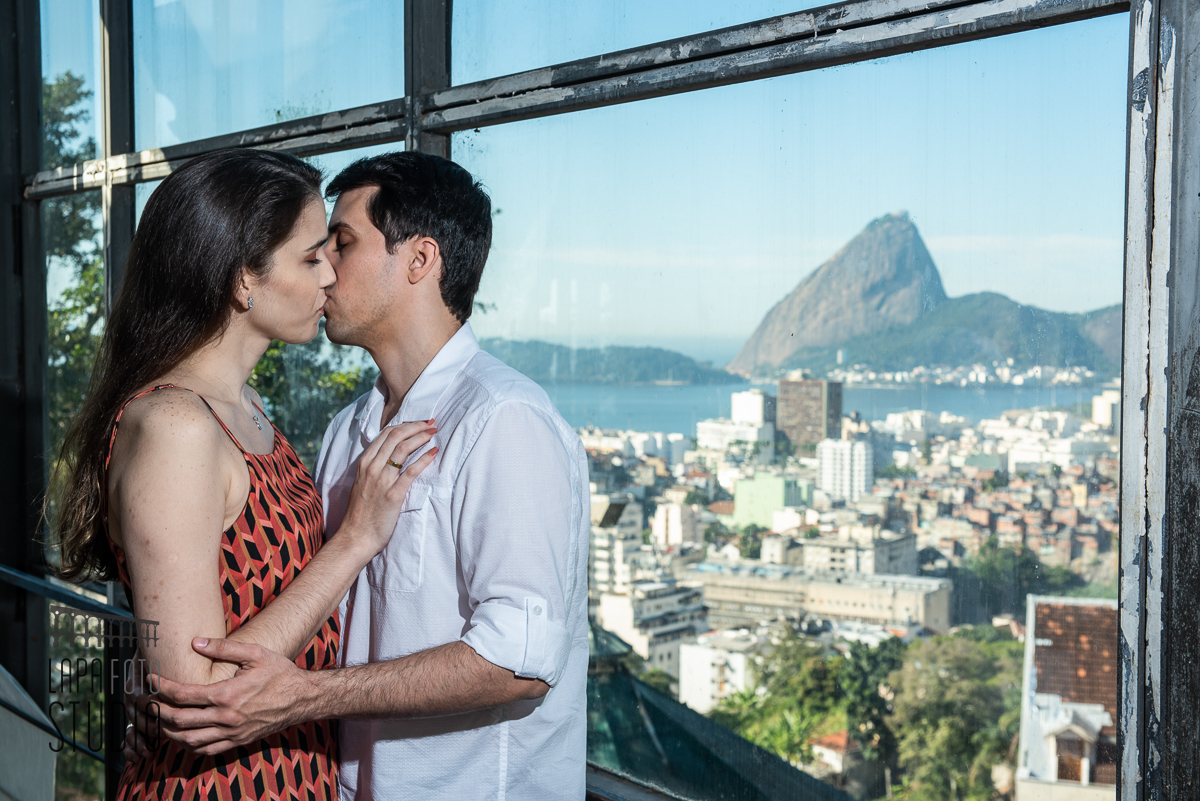 Noivos se beijam na janela de vidro com vista do Pão de Açúcar no pré wedding