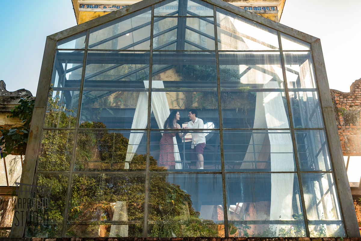 Noivos trocam carinhos na janela de vidro no pré wedding no Parque das Ruínas