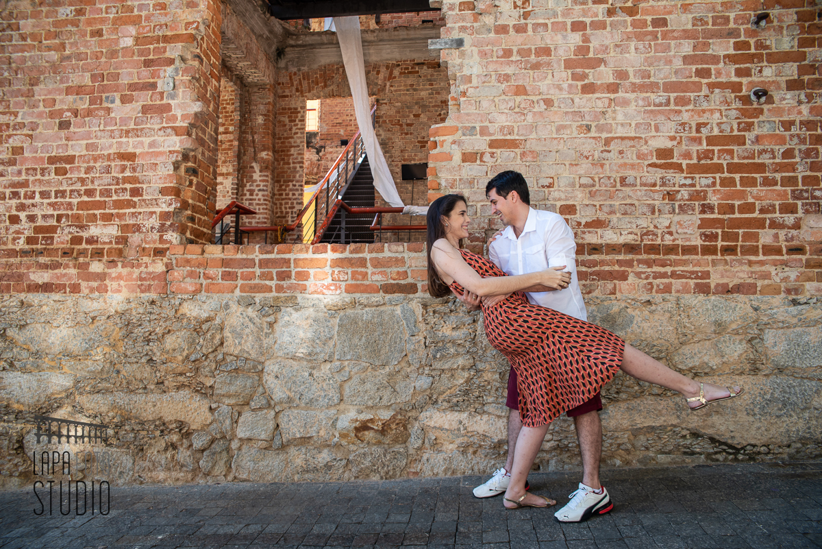 Noivos fazem pose de dança com parede de tijolos ao fundo no pré wedding no Parque das Ruínas