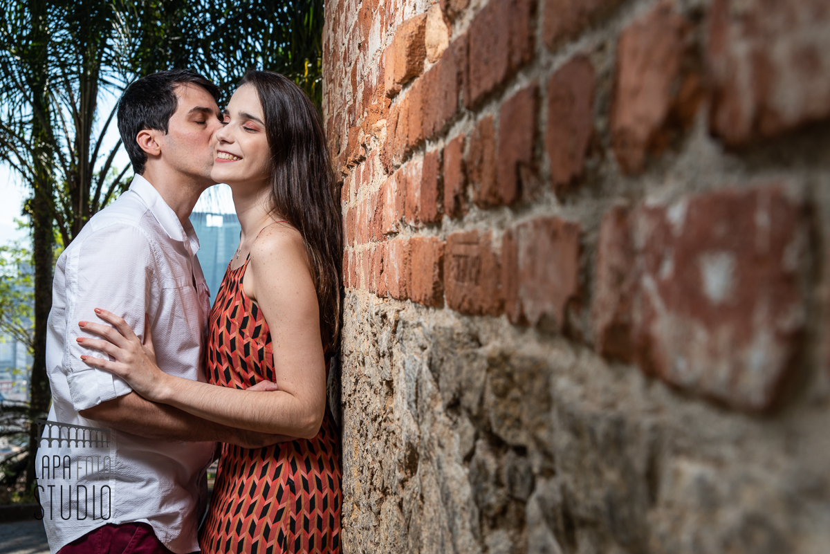 Noivo beija a noiva de olhos fechados encostados na parede de tijolinhos do Parque das Ruínas no ensaio pré casamento