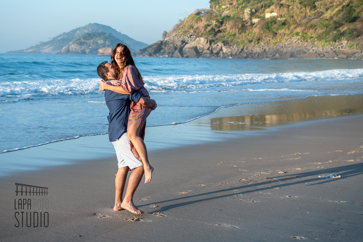 Noivo pega noiva no colo na beirada da praia no dia do pré wedding