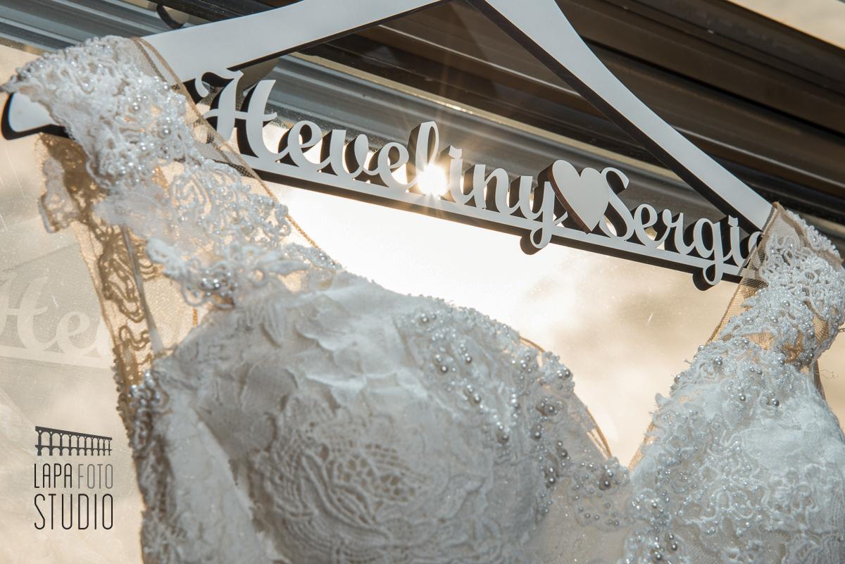 Vestido da noiva pendurado no cabide de casamento personalizado com sol ao fundo 