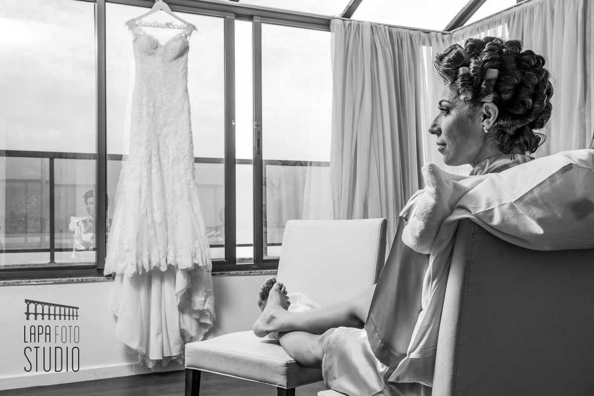 Foto em preto e branco da noiva no making of com vestido ao fundo