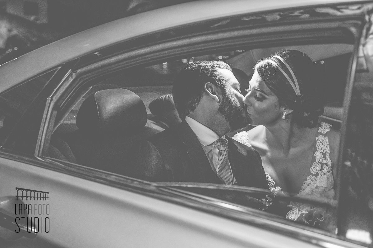 Foto em preto e branco dos noivos se beijando dentro do carro após cerimônia de casamento