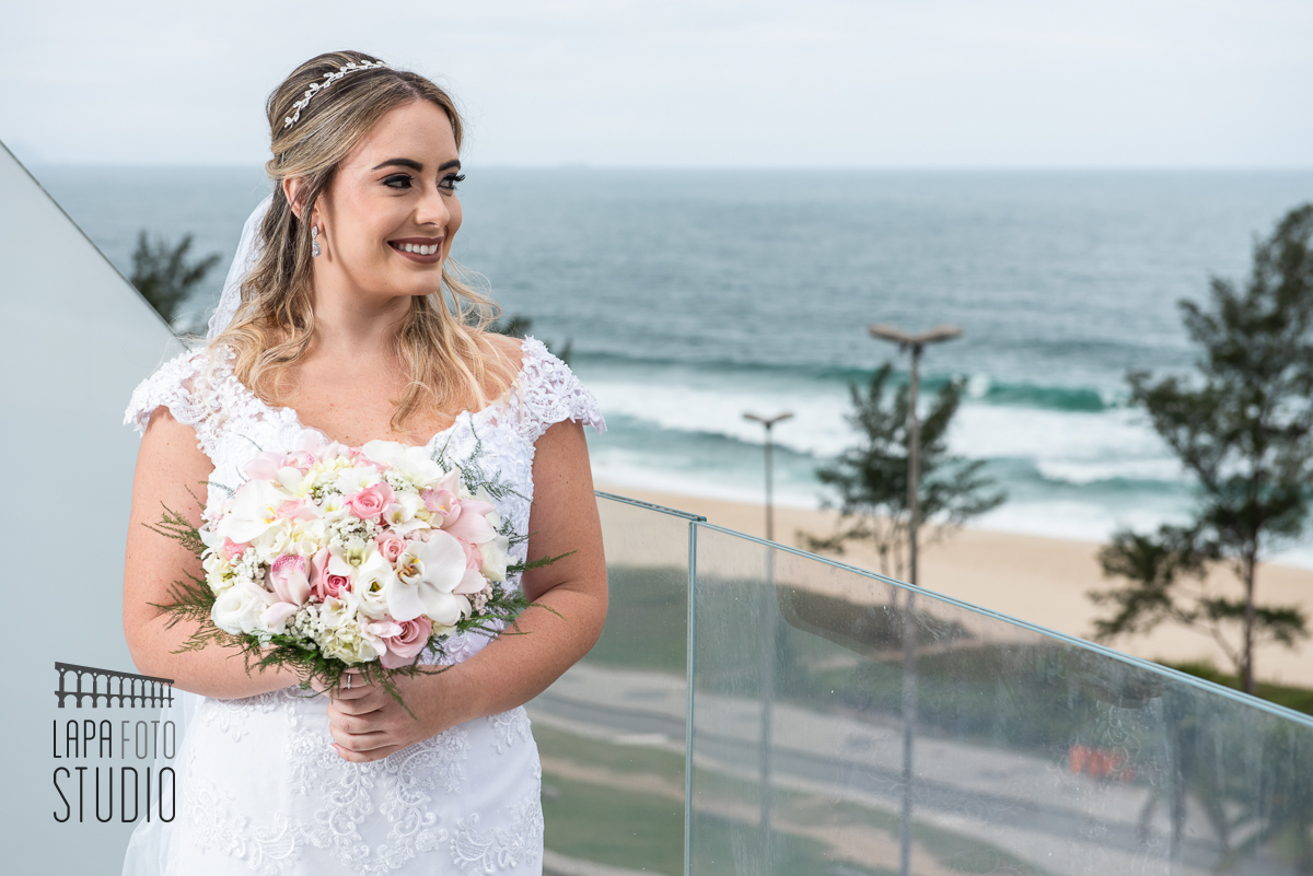 Noiva segura o buquê e sorri na varanda do hotel c design barra em frente a praia