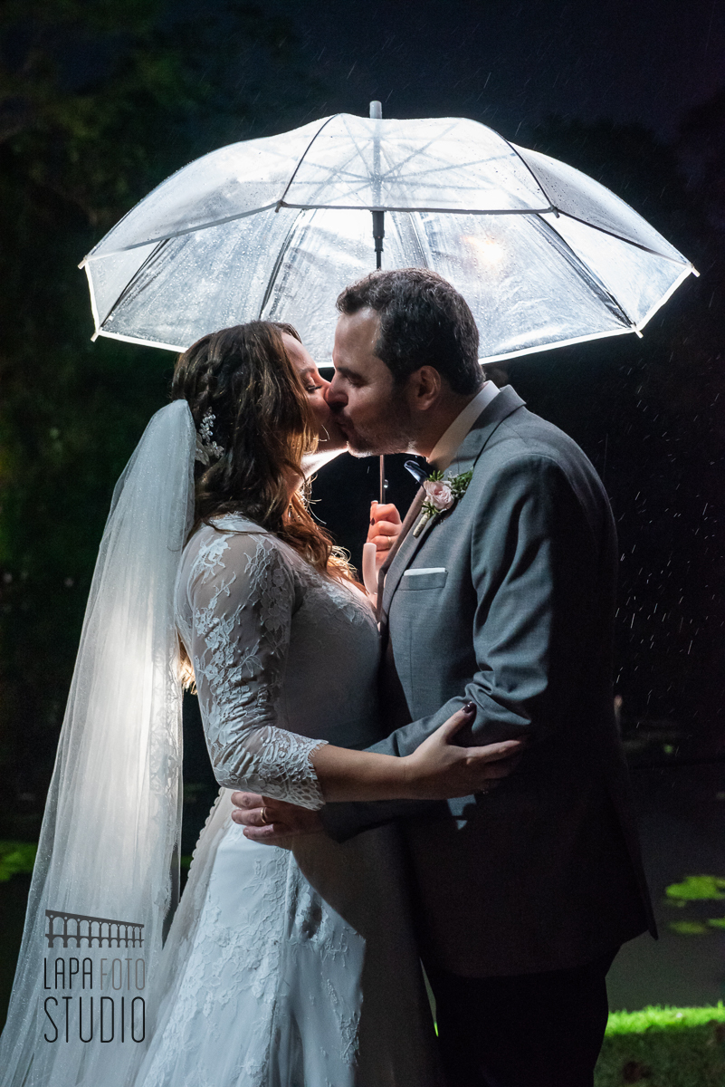 Noivos se beijam ,com guarda chuva em contra luz, após cerimônia de casamento no Sitio Meio do Mato