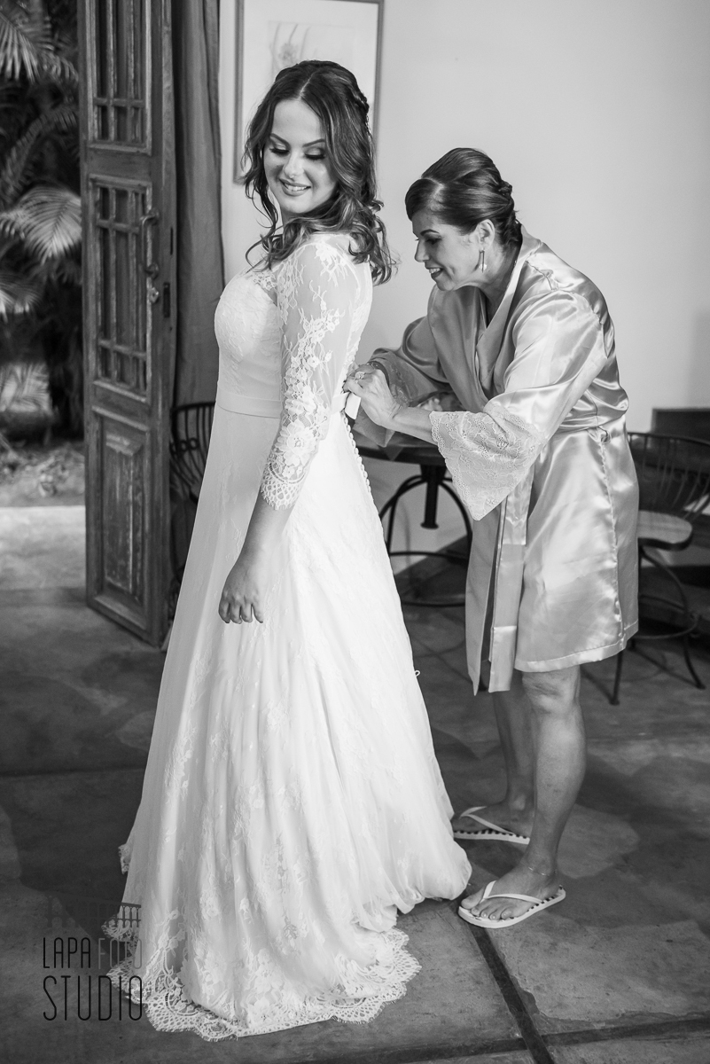 Foto em preto e branco da mãe da noiva fechando seu vestido no meio do mato eventos