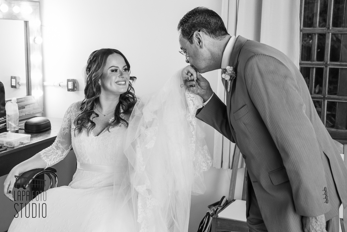 
Foto em preto e brando do pai beijando a  mão da noiva no making of no meio do mato eventos