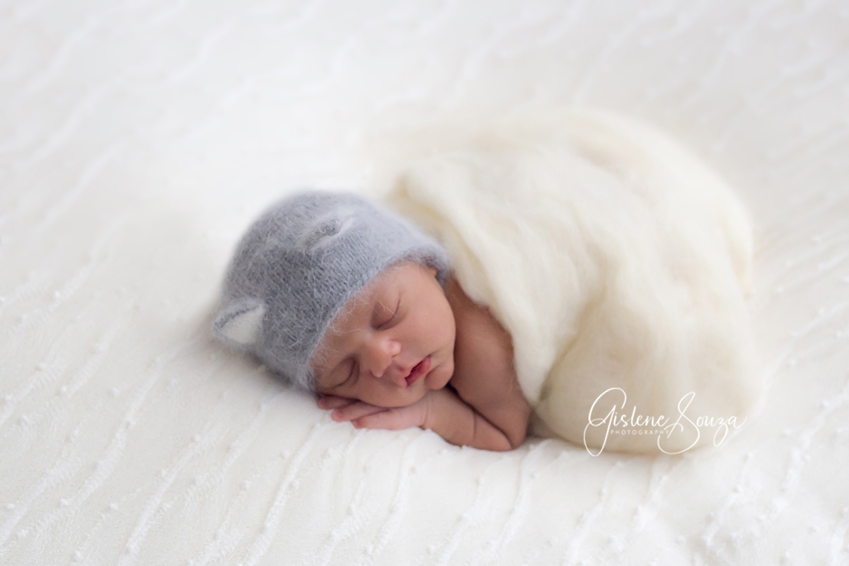 Ensaio de Newborn pose da bundinha no puff. Newborn com touca de gatinho nas cores cinza e braco.