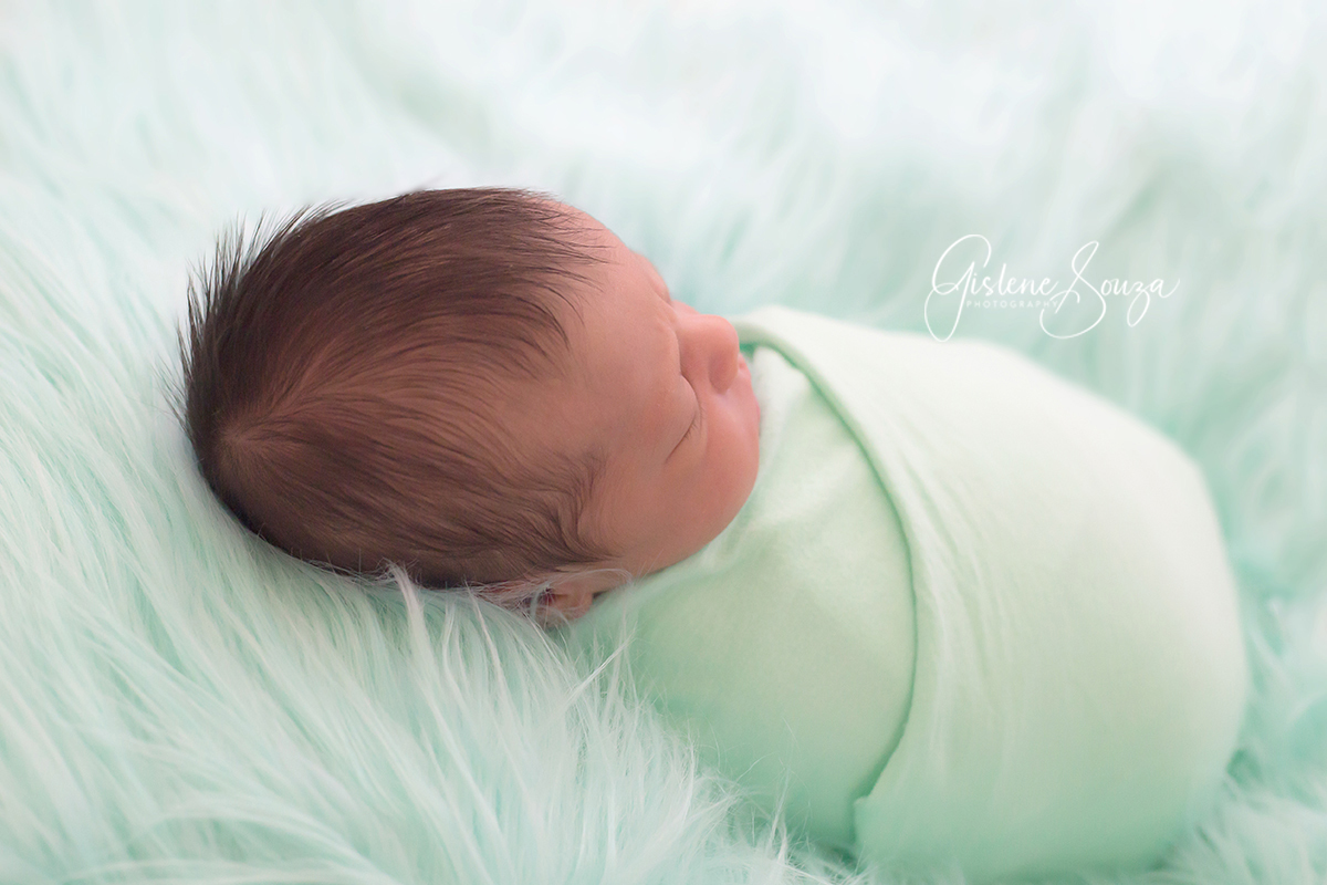 Ensaio de newborn no pelo verde sobre o puff. Pose enroladinho no wrap verde. Realizado em Belo Horizonte.