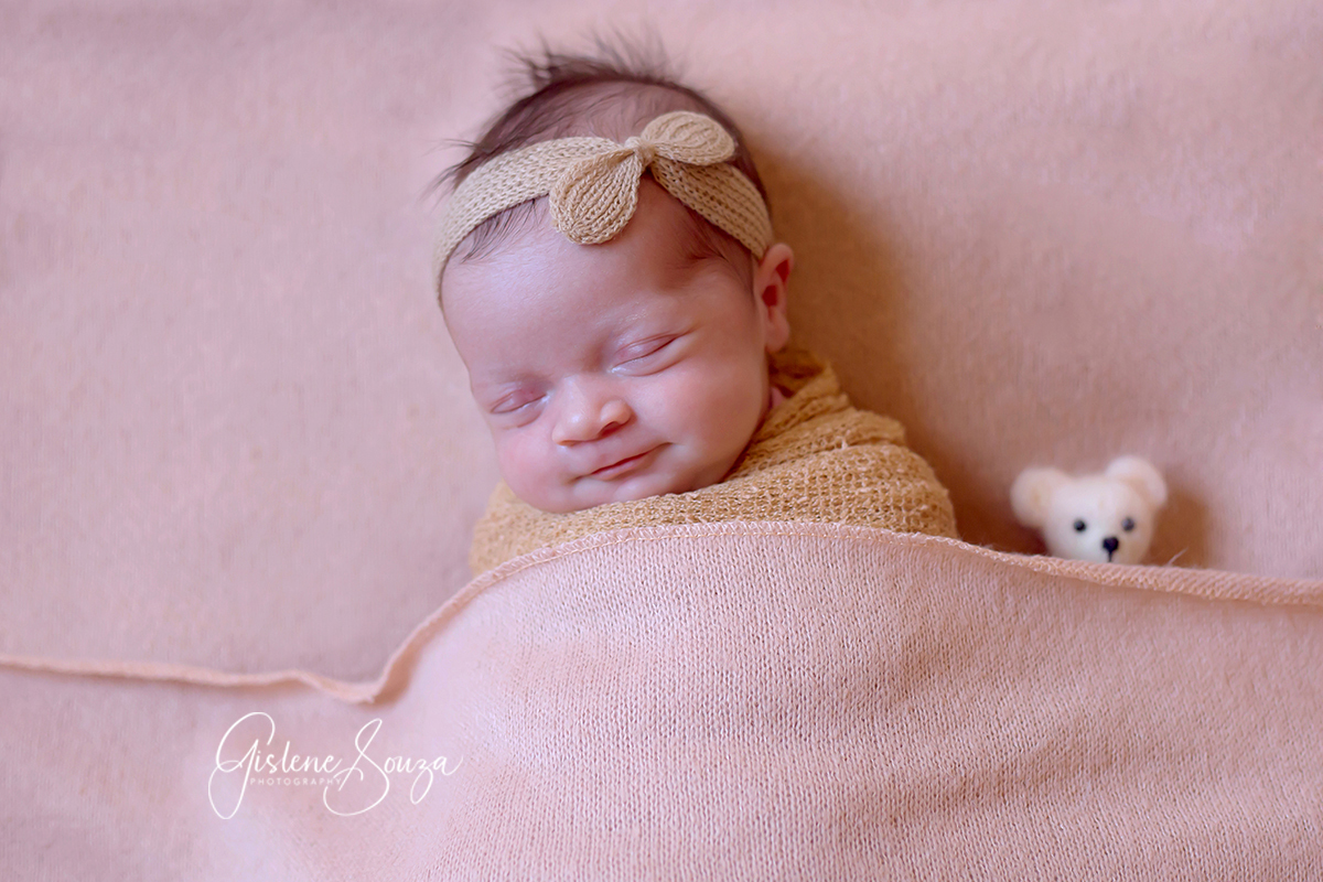 Fotografia de newborn em Pará de Minas. Ensaio newobrn pose de barriguinha para cima no puff com ursinho.